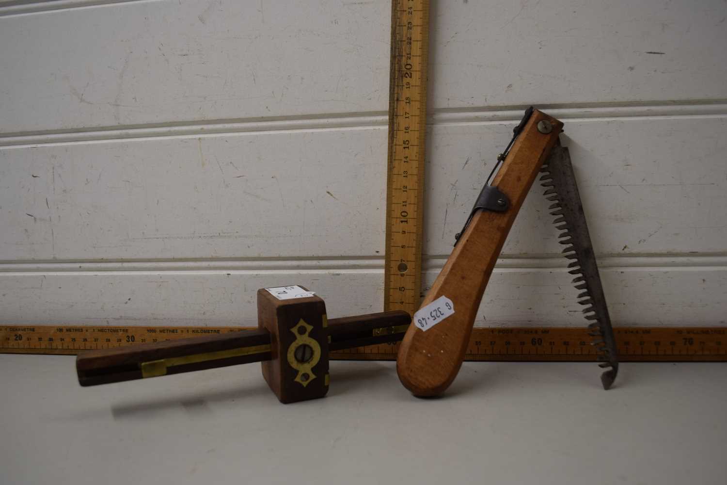 A folding pocket wooden handled tree saw and a wooden and brass gauge