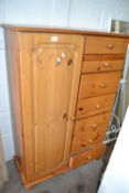 A pine bedroom cabinet with cupboard and shelves to one side and seven short drawers, 88cm wide