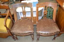 A pair of dining chairs with faux leather seats and casters