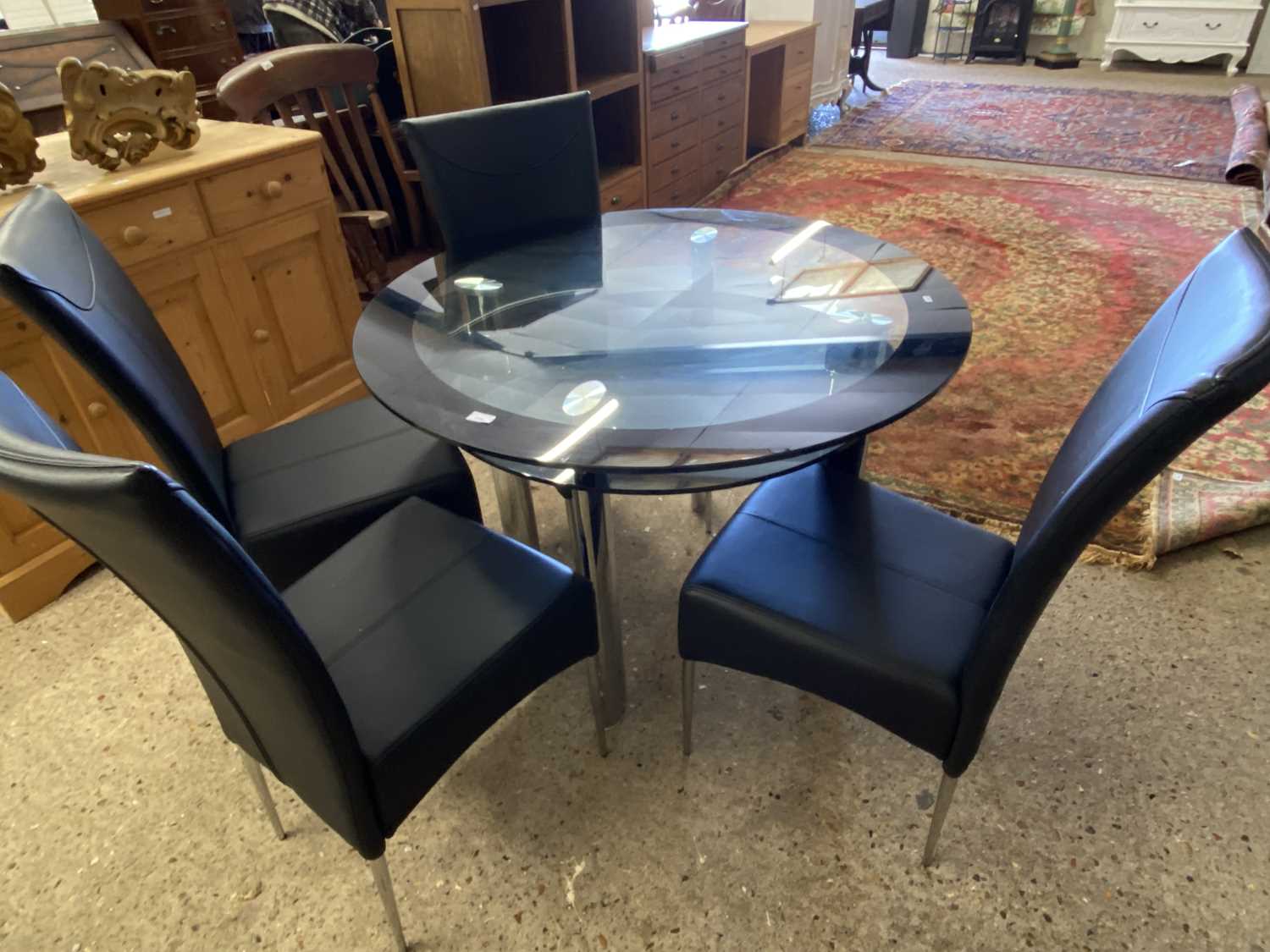 Modern circular glass top dining table and four accompanying black upholstered chairs