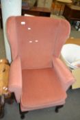 An apricot coloured upholstered wing back easy chair