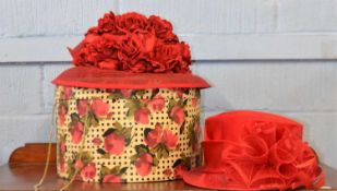 A vintage red hat box decorated with red roses containing a red silk and straw hat by Emma B for