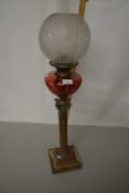 An oil lamp with brass base and red tinted glass font