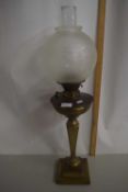 A brass oil lamp with frosted glass shade