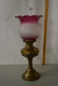 A brass based oil lamp with cranberry tinted shade