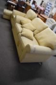 A three piece yellow suite comprising a two seater sofa, armchair and matching footstool