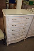 A cream and gilt decorated serpentine French style chest of drawers