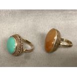 Two unmarked yellow metal poison rings, one set with amber, and one with turquoise cabochon, each