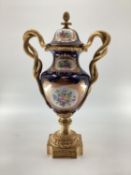 Meissen style lidded urn with gilt brass base and finial, gilt brass entwined snake handles, hand