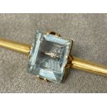 An unmarked yellow metal bar brooch, set with single emerald cut aquarmarine (12mm x 12mm) 7.8 g