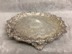 A Sterling silver salver with chased scrolling design and cast bolder raised on three feet by
