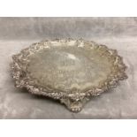 A Sterling silver salver with chased scrolling design and cast bolder raised on three feet by