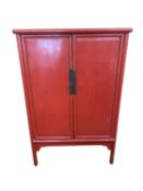 A C20th, Chinese style, two door cabinet on raised legs, with fitted interior, painted red 95cm W