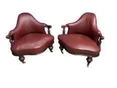 A pair of modern, wide seated and arched high back low arm chairs, in a dark red leather upholstery,