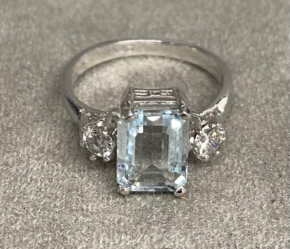 An 18ct white gold aquamarine and diamond ring. Emerald cut aqua with brilliant cut diamond accents.