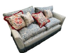A two seater sofa, with blue and cream upholstery and a quantity of decorative cushions, and fringed