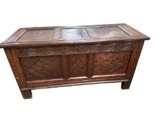 An oak three panelled coffer, with carving to front, and raised on square feet, 126cm W x 50cm D x