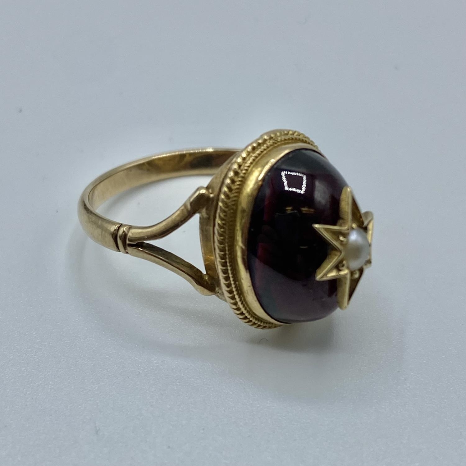 A Victorian unmarked yellow metal garnet and seed pearl dress ring, oval cabochon garnet with star