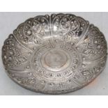 A repousse decorated white metal dish, inset with a coin to the centre, dia.17.5cm