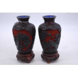 A pair of Chinese cinnibar type vases, each carved with flowers and upon a carved hardwood stand,