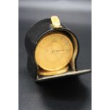 A Jaeger gilt brass cased travelling alarm clock, on oval plinth, h.4.9cm, with original leather