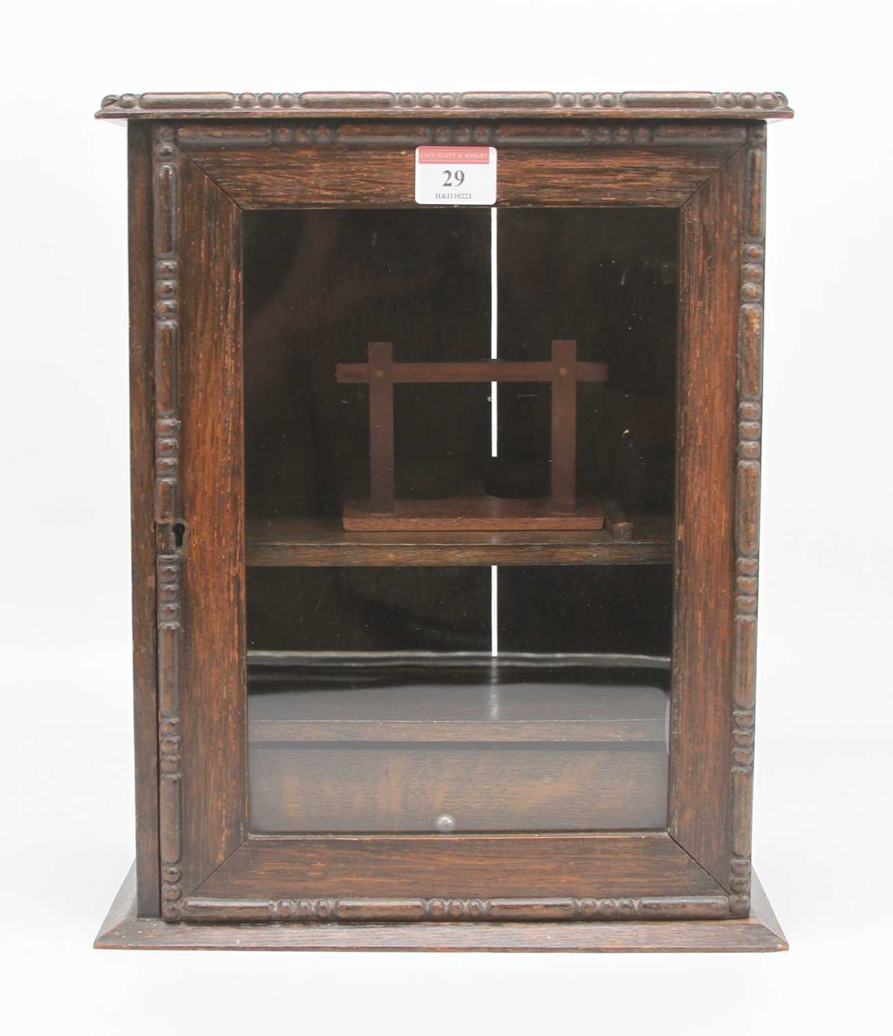 An early 20th century oak smoker's cabinet, the glazed door opening to reveal an arrangement of