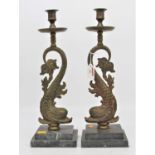 A pair of 19th century brass candlesticks, each in the form of a dolphin, mounted upon a stepped