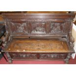 A late 19th century heavily carved three-panelled oak settle, the panelled back carved with