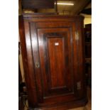 An early 19th century provincial oak single door hanging corner cupboard
