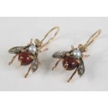 A pair of yellow metal winged insect drop earrings, each with a round cabochon cut garnet abdomen