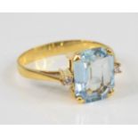 A yellow metal, aquamarine and diamond ring, featuring an emerald cut aquamarine with a round