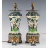 A pair of Chinese famille verte table lamps, each of baluster form upon figural supports, flanked by