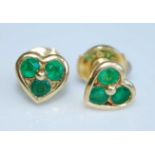 A pair of yellow metal heart shaped ear studs, each having three round faceted emeralds, with post