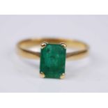 A yellow metal emerald single stone ring, the rectangular cut emerald in a four-claw setting,