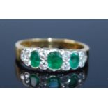A yellow metal, emerald and diamond half eternity ring, featuring three graduated oval emeralds
