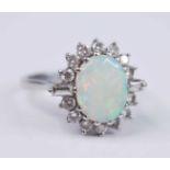 A white metal, opal and diamond oval cluster ring, comprising a centre oval cabochon cut opal within