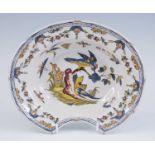 A French polychrome faience barber's shaving bowl, probably St Cloud, 18th century, decorated with a