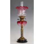 A Victorian brass oil lamp, the cranberry tinted glass shade above a similar glass font, spiral