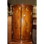 An early 19th century figured walnut double door bowfront hanging corner cupboard; together with