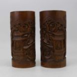 A pair of Chinese bamboo brush pots, each carved with various figures within pagodas and landscapes,