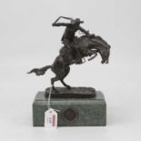 After Frederick Remington - a bronzed model of a cowboy on horseback, on naturalistic base,