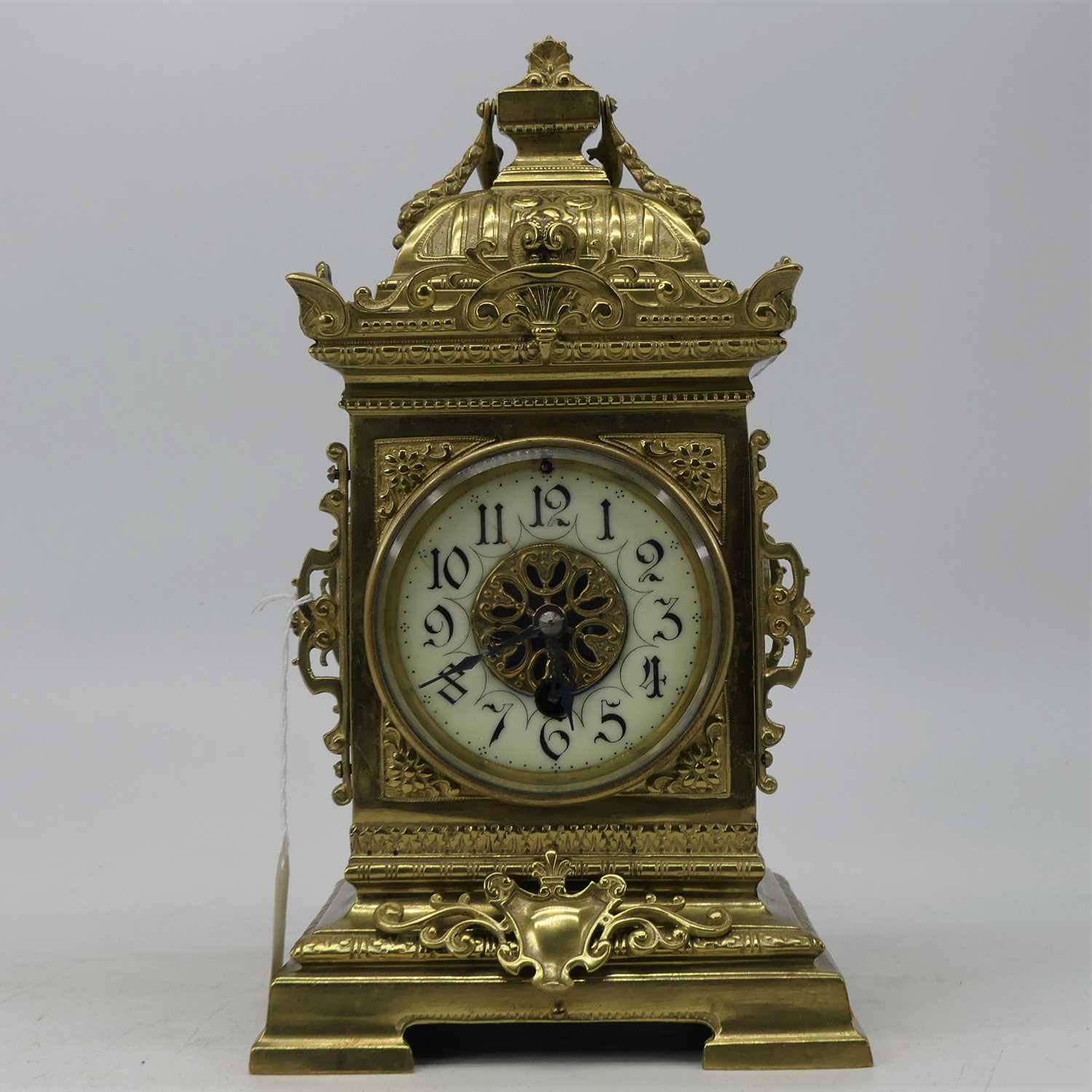 A late 19th century brass cased mantel clock, having a caddy-type top above an enamelled chapter