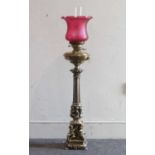 A large Victorian style brass oil lamp having a cranberry glass shade above a brass font on a fluted