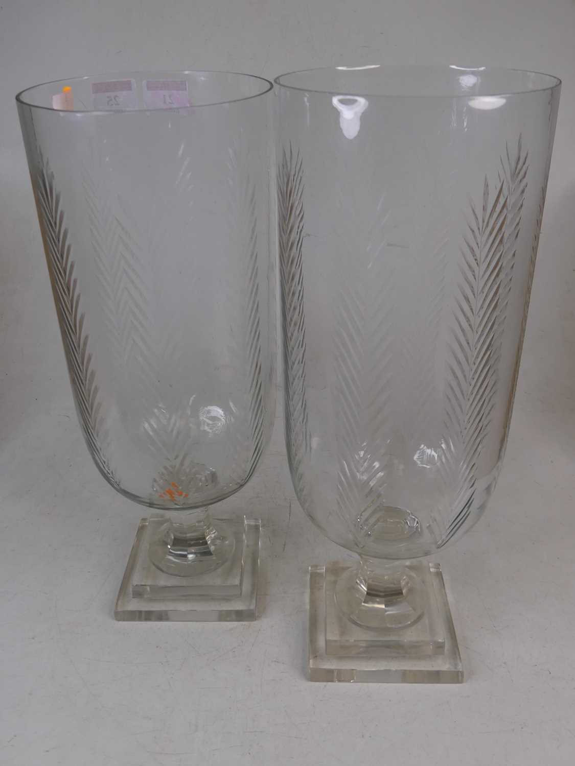 A pair of modern glass storm lamps, each having a cut glass body on facet cut stem and square