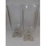 A pair of modern glass storm lamps, each having a cut glass body on facet cut stem and square