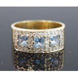 A yellow metal topaz dress ring, comprising three centre princess cut blue topaz within a border