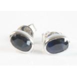 A pair of white metal sapphire single stone stud earrings, each featuring an oval faceted sapphire