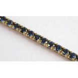 A yellow metal sapphire line bracelet featuring 55 round facetted sapphires in claw settings with