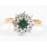 An 18ct yellow and white gold, emerald and diamond circular cluster ring, featuring a centre round