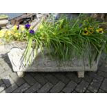 A large reconstituted stone rectangular garden trough planter, raised on squat end feet, the front